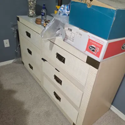 Sale Photo Thumbnail #7: Off-white textured laminate double dresser with bronze-tone metal handles and corner brackets, topped with shoe boxes and small decor.