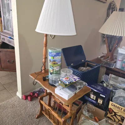 Sale Photo Thumbnail #29: Vintage wooden side table with integrated magazine rack, topped with a traditional table lamp and various household goods.
