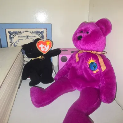 Sale Photo Thumbnail #109: Ty Beanie Babies Millennium magenta bear and small black bear sitting on a shelf alongside decorative items.