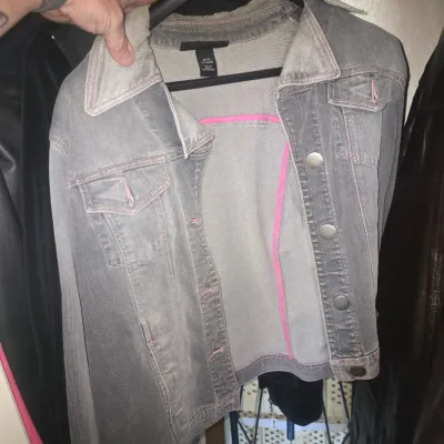 Sale Photo Thumbnail #63: Grey denim jacket featuring pink contrast stitching, metal buttons, and dual chest flap pockets, displayed on a hanger.