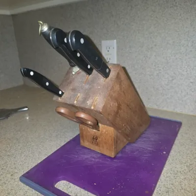 Sale Photo Thumbnail #123: J.A. Henckels wooden knife block with select kitchen knives, kitchen shears, and sharpening steel, resting on a purple plastic cutting board.