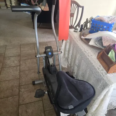 Sale Photo Thumbnail #95: Compact stationary exercise bike with a padded seat cover, digital display console, dual moving handlebars, and an attached red resistance band.