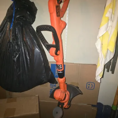 Sale Photo Thumbnail #79: Black & Decker electric string trimmer and edger hanging in storage, showing moderate wear from use.