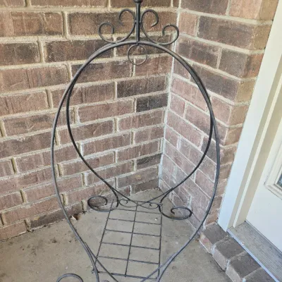 Sale Photo Thumbnail #127: Black wrought iron firewood log rack featuring scrollwork accents, a central shelf, and a top finial.
