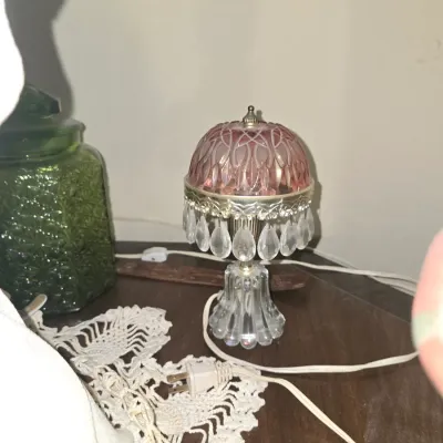 Sale Photo Thumbnail #48: Vintage small accent lamp featuring a pink pressed-glass dome shade with hanging crystal prisms and a clear glass base, displayed alongside a green glass jar and crocheted doily.