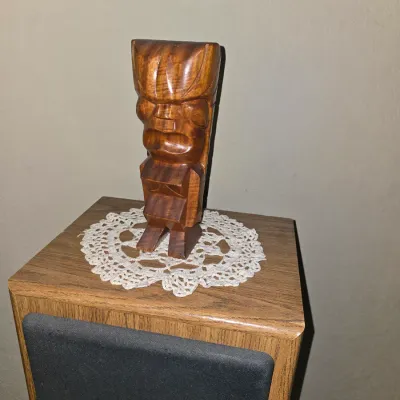 Sale Photo Thumbnail #51: Vintage hand-carved wooden tiki statue, displayed on a crocheted lace doily atop a wood-grained speaker cabinet.