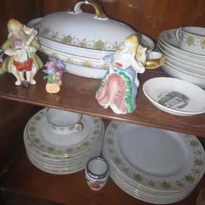 Sale Photo Thumbnail #88: Vintage gold-trimmed porcelain dinnerware set with matching covered tureen, paired with small painted ceramic figurines inside a wooden cabinet.