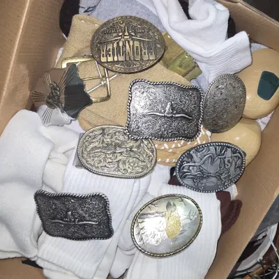 Sale Photo Thumbnail #2: Cardboard box containing a collection of vintage Western metal belt buckles mixed with socks and small accessories.
