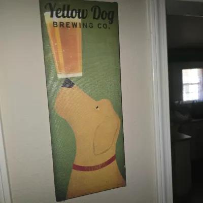 Sale Photo Thumbnail #68: Vertical canvas wall sign featuring Yellow Dog Brewing Co. artwork, depicting a dog balancing a pint of beer on its nose.