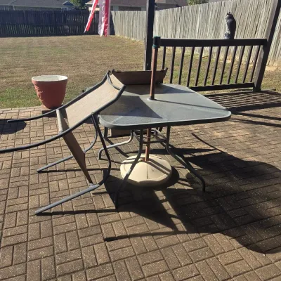 Sale Photo Thumbnail #100: Outdoor patio dining table with a tempered glass top and umbrella base, accompanied by mesh lawn chairs on a paved backyard patio.