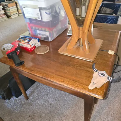 Sale Photo Thumbnail #57: Mid-century modern wooden end table featuring tapered legs, holding a wooden base table lamp, a ceramic bull skull figurine, and miscellaneous office supplies.