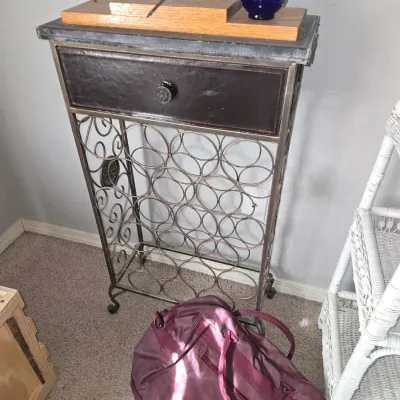 Sale Photo Thumbnail #23: Rustic wrought iron wine rack table featuring a leather-front drawer and a cobalt blue perfume bottle displayed on top.