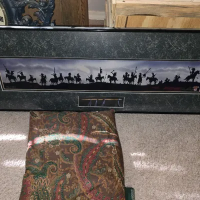Sale Photo Thumbnail #21: Framed panoramic Western art print featuring silhouettes of Native American horseback riders, numbered 156/250, presented above a paisley throw pillow.