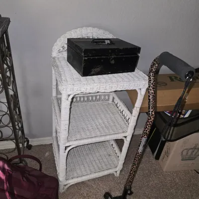 Sale Photo Thumbnail #26: White woven wicker three-tiered shelving unit, topped with a vintage black metal cash box.