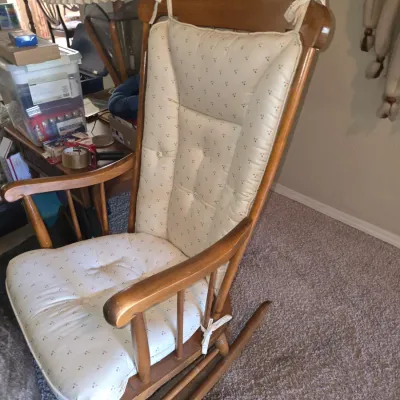 Sale Photo Thumbnail #59: Vintage wooden rocking chair featuring a high back and tied cream cushions with a small floral pattern.