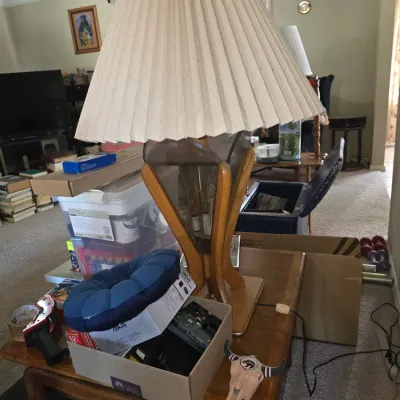 Sale Photo Thumbnail #58: Mid-century modern table lamp featuring a wooden frame, smoked glass accents, and a large pleated fabric shade, resting on a wooden side table.