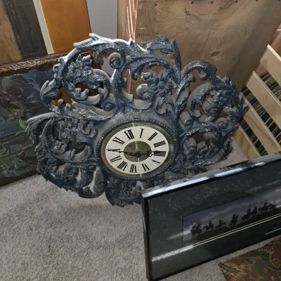 Sale Photo Thumbnail #20: Ornate Baroque-style New Haven wall clock with an intricate scrollwork frame, displayed alongside framed artwork and a wooden crate.