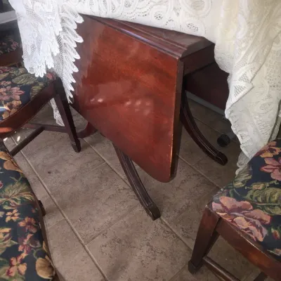 Sale Photo Thumbnail #85: Traditional mahogany drop-leaf dining table with pedestal base, covered with a white lace tablecloth, paired with floral upholstered chairs.