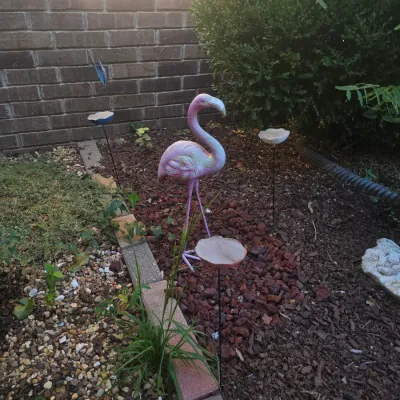 Sale Photo Thumbnail #125: Pink painted metal flamingo garden statue set in a mulched flower bed among decorative flower stakes.