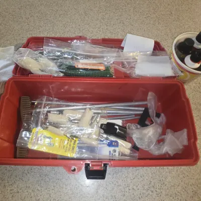 Sale Photo Thumbnail #105: Red plastic toolbox filled with gun cleaning supplies, including cleaning rods, patches, brushes, and various liquid solvents and oils.