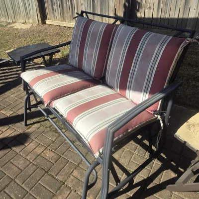 Sale Photo Thumbnail #98: Outdoor metal patio glider bench featuring red, beige, and grey striped cushions.