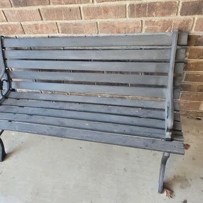 Sale Photo Thumbnail #126: Outdoor park bench featuring a black cast iron frame with decorative scrollwork armrests and dark painted wooden slats.
