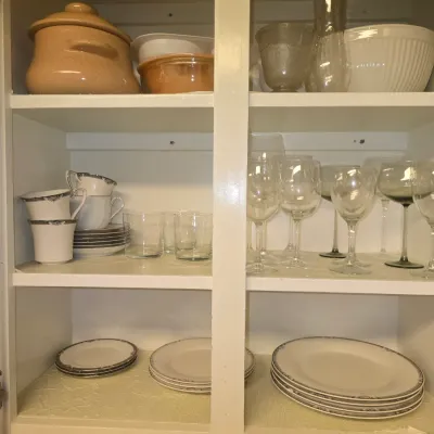 Sale Photo Thumbnail #118: White kitchen cabinet filled with glassware, teacups, saucers, plates, and ceramic cookware.