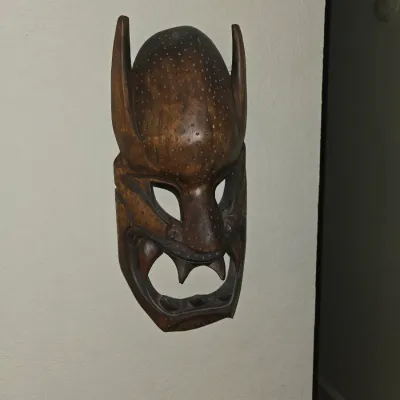 Sale Photo Thumbnail #52: Hand-carved dark wood ceremonial style mask with horns, stippled texture, and exaggerated facial features, mounted as wall decor.
