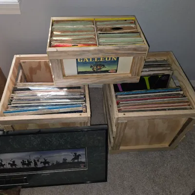 Sale Photo Thumbnail #22: Collection of vintage vinyl records and 45 RPM singles stored inside three wooden crates, shown alongside a framed silhouetted art print.