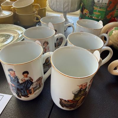 Sale Photo Thumbnail #21: Collection of porcelain Norman Rockwell illustration mugs with gold rims, accompanied by yellow mid-century tableware and vintage tins.