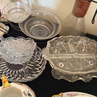 Sale Photo Thumbnail #32: Collection of vintage clear glassware, including pressed glass bowls and serving dishes, a mid-century glass carafe with a striped neck, and floral china teacups.