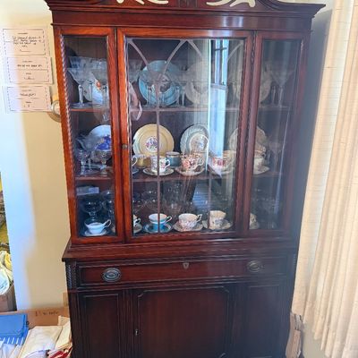 Sale Photo Thumbnail #33: Traditional mahogany china cabinet with a swan-neck broken pediment top, glazed mullion doors, and bottom storage cabinet, filled with glassware and china.