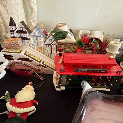 Sale Photo Thumbnail #57: Collection of San Francisco-themed decor and Christmas collectibles, including a ceramic San Francisco street scene sculpture, a red Powell & Hyde Sts. trolley car, Santa ornaments, and milk glass items.