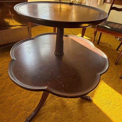 Sale Photo Thumbnail #51: Vintage dark mahogany two-tier dumbbell accent table featuring a scalloped lower shelf, rounded top tier, and carved tripod pedestal base with surface wear.
