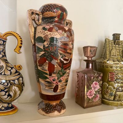 Sale Photo Thumbnail #40: Collection of vintage decorative ceramics including an Italian majolica style pitcher, an ornate Satsuma Moriage urn vase, a floral painted glass decanter, and a cottage-shaped cookie jar.
