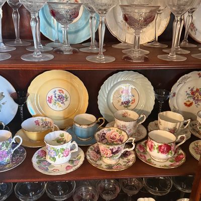 Sale Photo Thumbnail #34: Collection of vintage etched stemware, floral china teacups, saucers, and decorative cabinet plates displayed on wooden shelves.