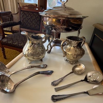 Sale Photo Thumbnail #44: Vintage silver-plate hollowware set featuring an ornate chafing dish, water pitchers, ladles, and serving utensils.