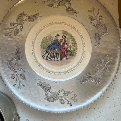 Sale Photo Thumbnail #15: Vintage forged aluminum charger featuring a central porcelain insert with a Victorian scene of women and a child, surrounded by a floral and berry motif.