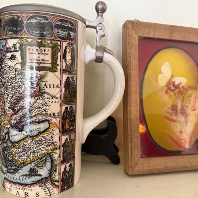 Sale Photo Thumbnail #38: Ceramic lidded beer stein featuring a vintage European map motif, displayed alongside a framed shadowbox with dried flowers and a preserved white butterfly.