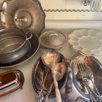 Sale Photo Thumbnail #18: Collection of vintage serveware, including tarnished silver-plated serving dishes, ladles, a covered butter dish, and a white milk glass deviled egg platter.