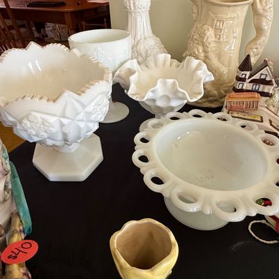 Sale Photo Thumbnail #59: Collection of mid-century milk glass glassware, including a open-work lace edge bowl, ruffle edge pedestal dish, and embossed compotes, alongside vintage ceramic pitchers and decorative items.