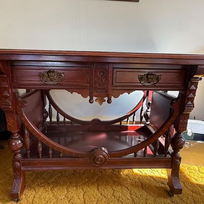 Sale Photo Thumbnail #54: Antique carved dark wood library table featuring ornate drawer pulls, turned spindle accents, and a curved lower shelf design.