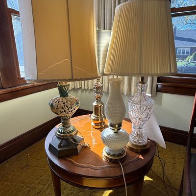 Sale Photo Thumbnail #53: Collection of vintage table lamps displayed on a round inlaid wood side table, including a cut crystal lamp, a white hobnail milk glass lamp, and an ornate ceramic lamp.