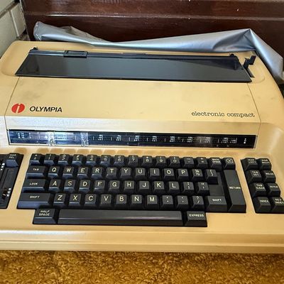 Sale Photo Thumbnail #63: Vintage Olympia Electronic Compact typewriter in a tan casing, complete with a black keyboard and clear paper guide.