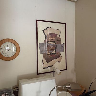 Framed abstract collage art piece hanging on a wall alongside a round wooden wall clock.