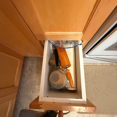 Open wooden kitchen drawer containing assorted baking utensils, including a wooden rolling pin and mesh strainers.
