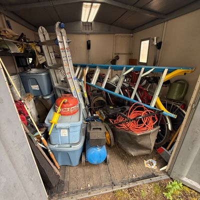 Storage shed contents including aluminum folding step ladders, extension ladders, a portable air compressor, plastic totes, garden...