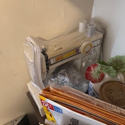 Vintage white sewing machine in a clear zippered vinyl storage cover, sitting alongside office and craft supplies.