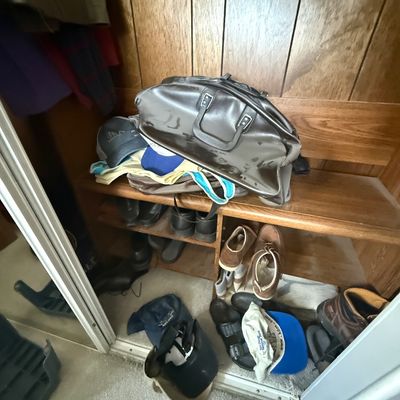 Vintage dark gray metallic duffel bag resting on a wooden closet shoe rack alongside various baseball caps and men's footwear.