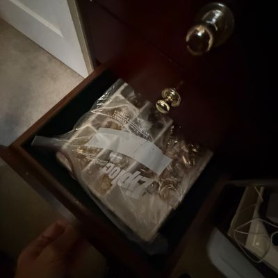 Open dark wood dresser drawer containing a plastic bag filled with various jewelry pieces.
